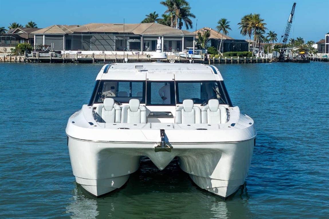 A sleek white boat with cushioned seats floats on clear blue water, near waterfront homes and palm trees.